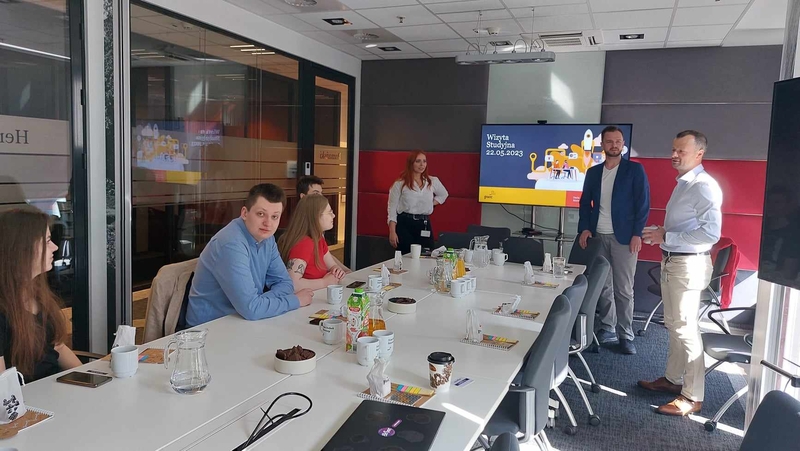 Mapa Biznesowa Łodzi - Wizja Lokalna - PwC - dwoje pracowników firmy rozmawia ze studentami uczestniczącymi w spotkaniu, w większości siedzącymi przy stole