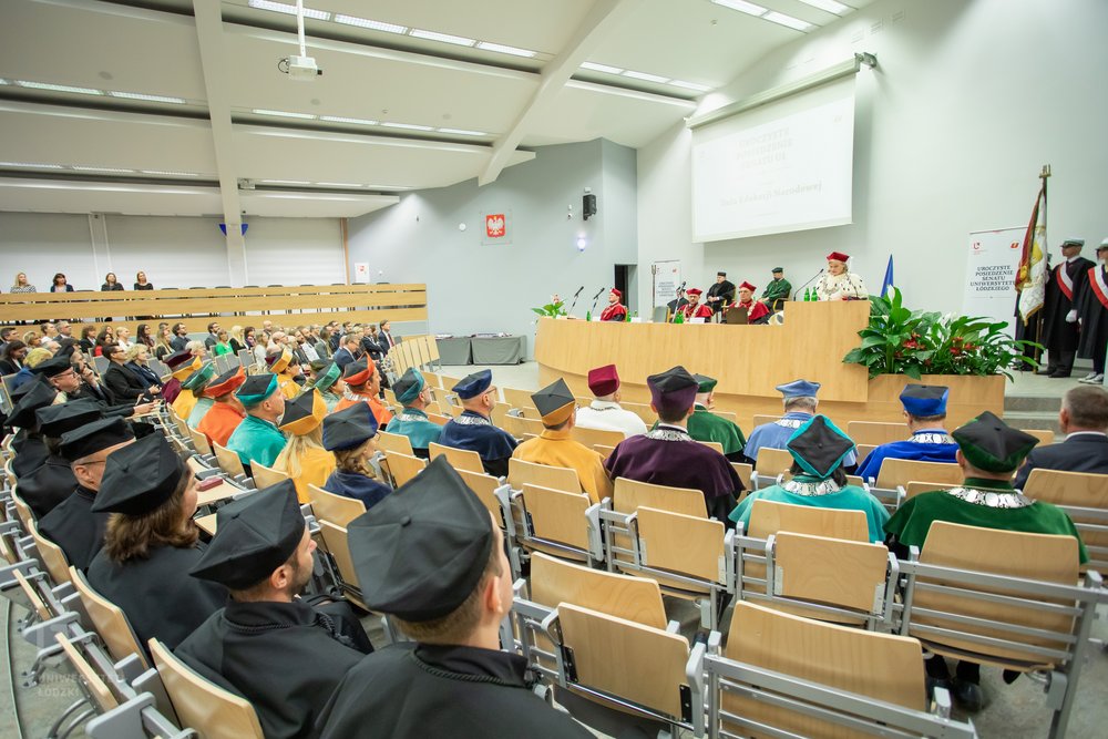 Zdjęcie dużej sali wykładowej, na podwyższeniu władze Wydziału w formalnych strojach, przed nimi zgromadzona publiczność