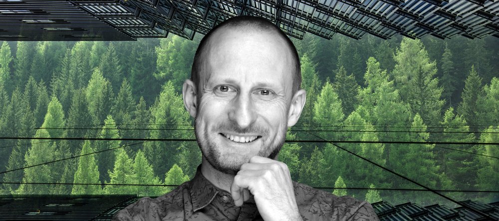 Uśmiechnięty wizerunek profesora Jakuba Kronenberga na tle zielonych drzew, widoczne również szklane fasady drapaczy chmur