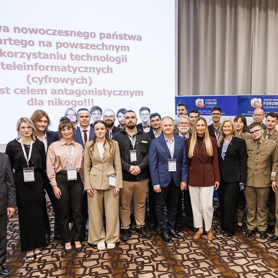 Grupowe zdjęcie laureatów, organizatorów i uczestników 32. Forum Teleinformatyki. Uczestnicy stoją w kilku rzędach na tle ekranów z logotypami Forum i hasłem wydarzenia.
