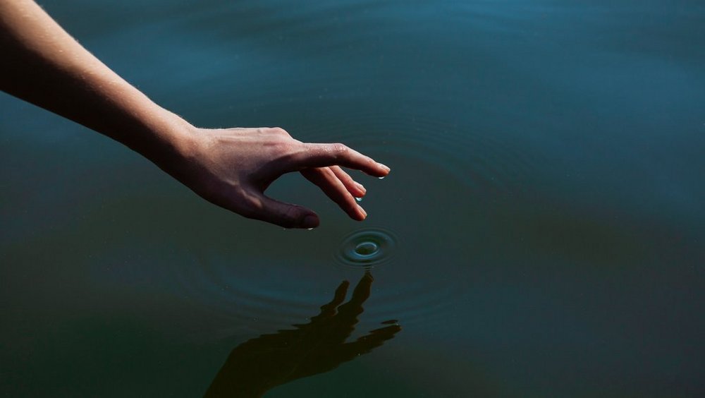 Zdjęcie rzeki i dłoni z zanurzanym w wodzie palcem 