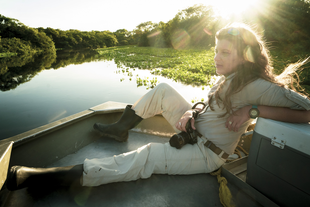 Dr Izabela Stachowicz sitting comfortably in a boat sailing on a river among the jungle. She is holding a camera in her hand.