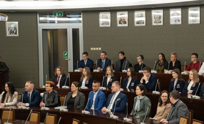 Grupa uczniów i wykładowców w auli akademickiej.