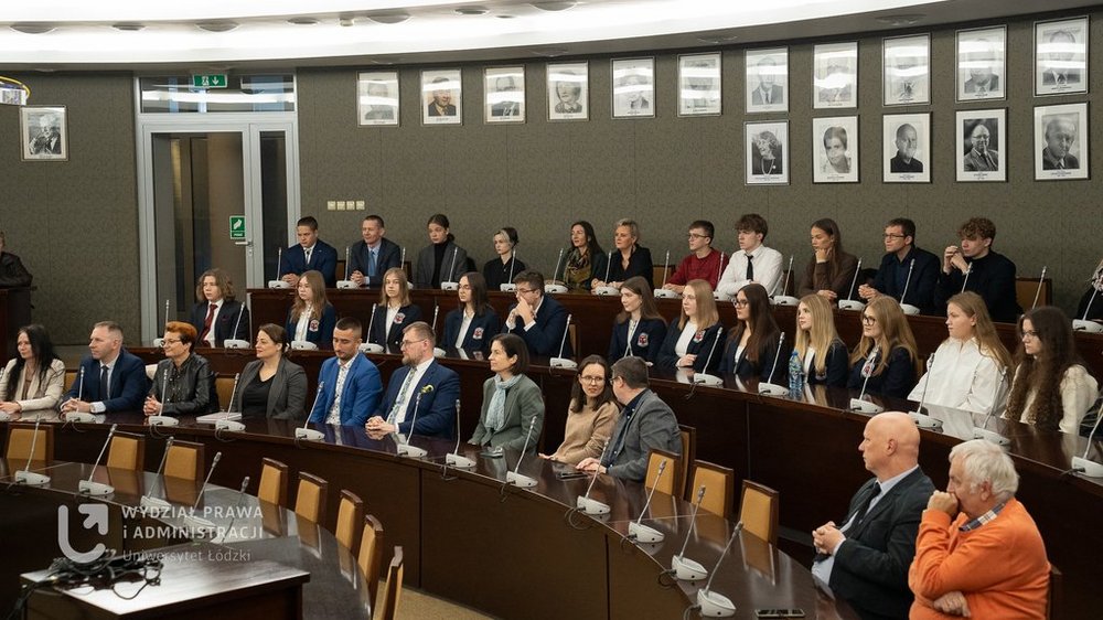 Grupa uczniów i wykładowców w auli akademickiej.