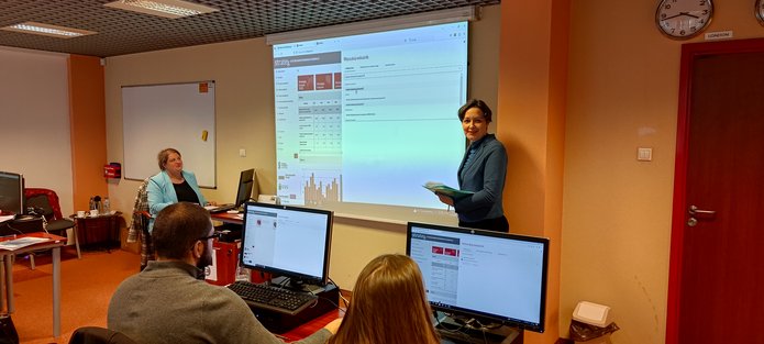 Dwie pracowniczki Urzędu Statystycznego w Łodzi z uśmiechem prezentują działanie systemu Strateg; uczestnicy szkolenia odtwarzają na swoich komputerach to, co Prowadzące pokazały na dużym ekranie