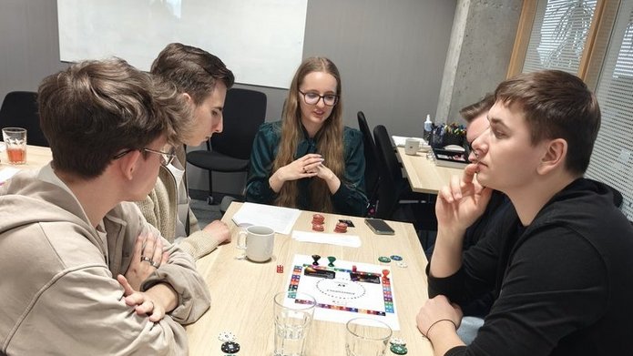 wizja llokalna w EY - studenci EkSocu siedzprzy stole w siedzibie EY i rozmawiają i grają w grę planszową