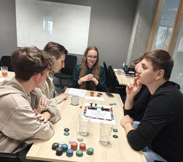 wizja llokalna w EY - studenci EkSocu siedzprzy stole w siedzibie EY i rozmawiają i grają w grę planszową