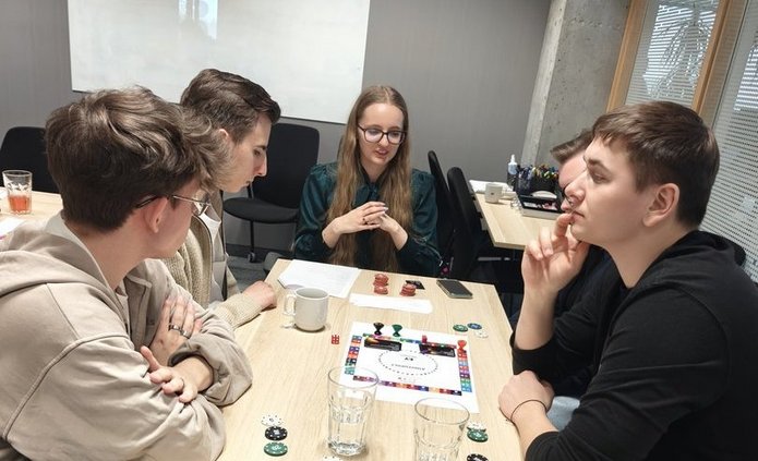wizja llokalna w EY - studenci EkSocu siedzprzy stole w siedzibie EY i rozmawiają i grają w grę planszową