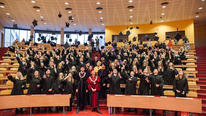 młodzi ludzie w togach rzucający biretami