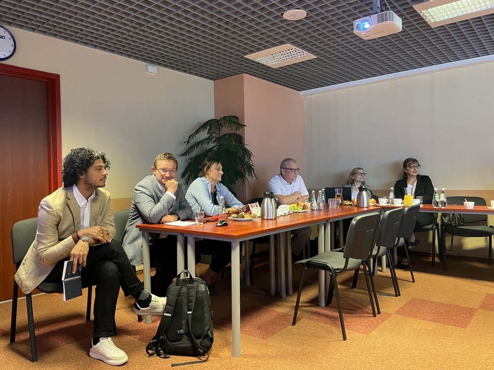 grupa ludzi siedząca przy stołach z poczęstunkiem i laptopami