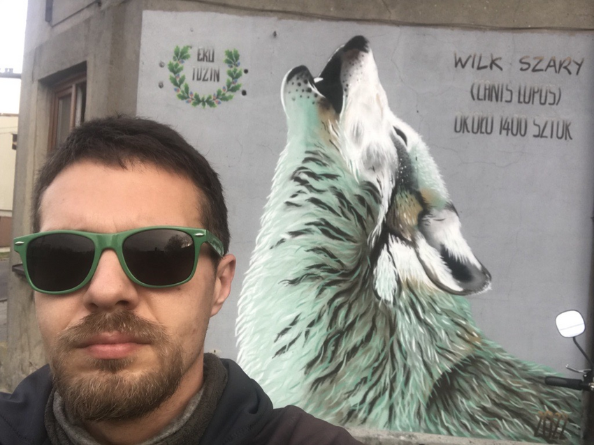 A man wearing glasses with a poster with a wolf in the background