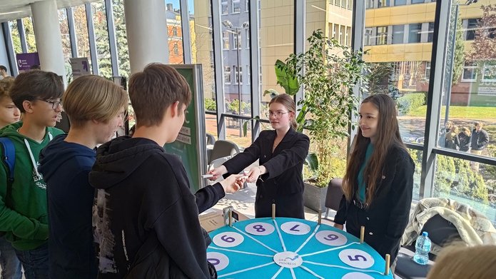 drzwi otwarte 2025 - dwie studentki SKN Progress rozdają nagrody uczniom ustawionym w kolejce przed stoiskiem EKO EkSoc