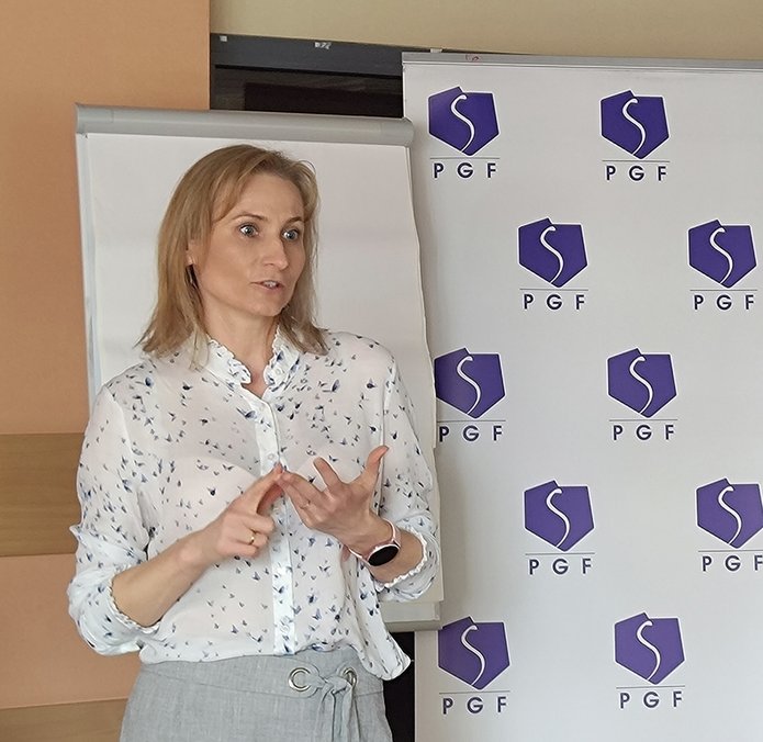 szkolenie pt. Autoprezentacja i radzenie sobie ze stresem - Polska Grupa Farmaceutyczna - 14.04.2025 - Prowadząca szkolenie stoi na tle rollupów PGF i Wydziału Ekonomiczno-Socjologicznego UŁ