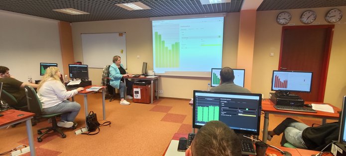 uczestnicy szkolenia, siedząc przy komputerach, słuchają Prowadzącej szkolenie, prezentującej działanie systemu Strateg na dużym ekranie