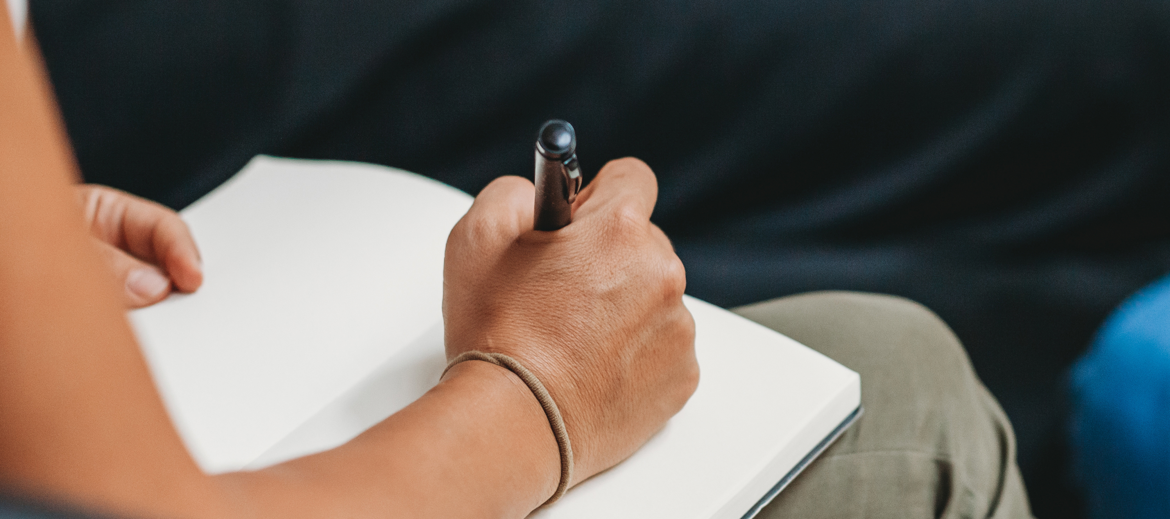 Osoba pisząca długopisem w notesie; widoczna ręka trzymająca długopis nad otwartą, pustą kartką